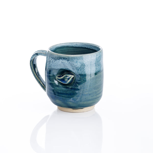 Handmade ceramic mug by Kristin Roach with a textured, swirled blue and teal glaze, featuring a small bird motif on the side. Part of the MOKA x KRISTIN ROACH POTTERY exclusive, limited edition collaboration